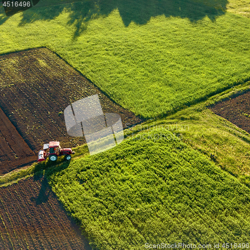 Image of Aerial view from the drone, a bird\'s eye view of agricultural fields with a road through and a tractor on it in the spring evening at sunset