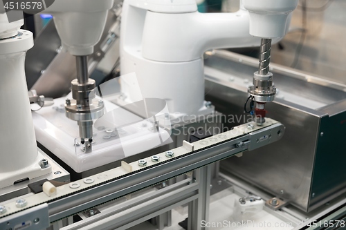 Image of Automatic robot arm working in industrial environment sorting out screws