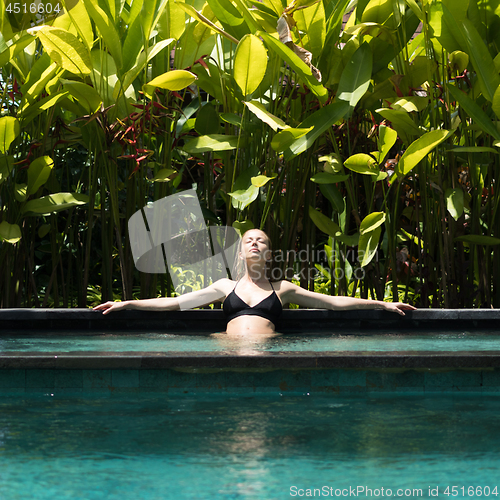 Image of Sensual young woman relaxing in outdoor spa infinity swimming pool surrounded with lush tropical greenery of Ubud, Bali.