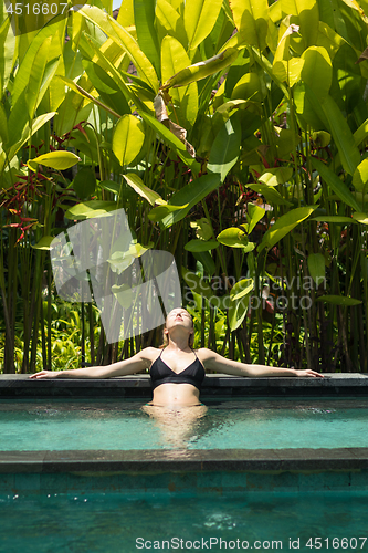 Image of Sensual young woman relaxing in outdoor spa infinity swimming pool surrounded with lush tropical greenery of Ubud, Bali.