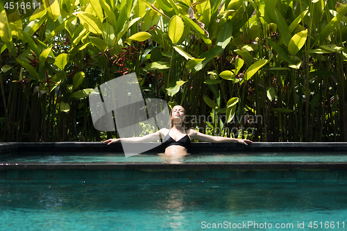 Image of Sensual young woman relaxing in outdoor spa infinity swimming pool surrounded with lush tropical greenery of Ubud, Bali.