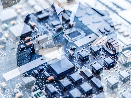 Image of Businessman standing with folded arms in a classic navy blue suit against pc motherboard chip photo layer.