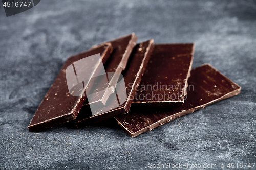 Image of Chunks of broken dark chocolate stacked on grey background.