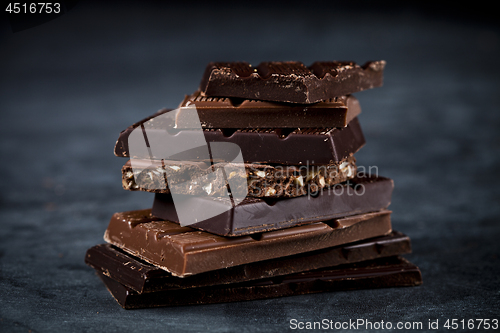 Image of Chocolate bars pieces stack on black background. Sweet food phot