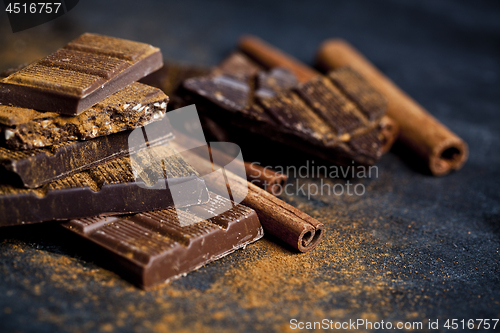 Image of Chocolate bars pieces heap witn cinnamon powder and sticks. 