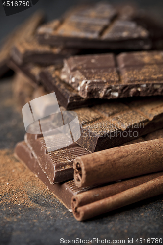 Image of Chocolate bar pieces heap witn cinnamon powder and sticks. Broke