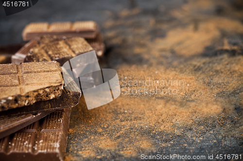 Image of Broken chocolate  witn cinnamon powder stacked on black backgrou