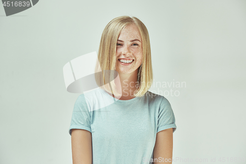 Image of The happy freckled woman standing and smiling against gray background.