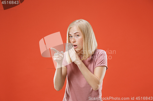 Image of The young woman whispering a secret behind her hand over red background