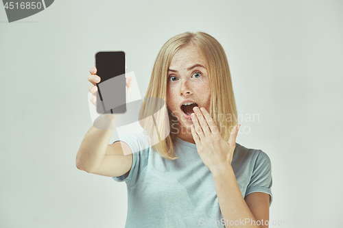 Image of Portrait of a confident casual girl showing blank screen mobile phone isolated over gray background