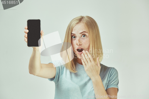 Image of Portrait of a confident casual girl showing blank screen mobile phone isolated over gray background