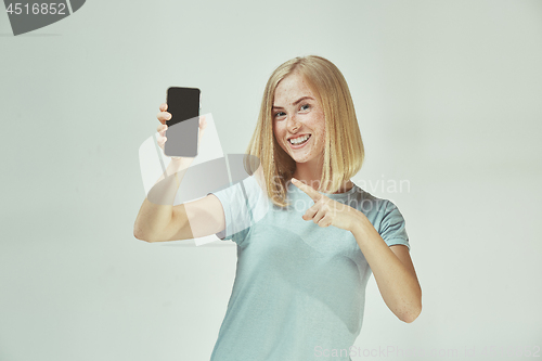 Image of Portrait of a confident casual girl showing blank screen mobile phone isolated over gray background