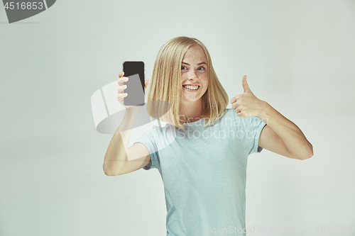 Image of Portrait of a confident casual girl showing blank screen mobile phone isolated over gray background