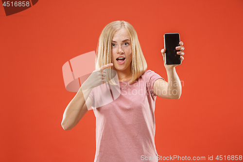 Image of Portrait of a confident casual girl showing blank screen mobile phone isolated over red background