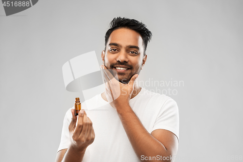 Image of smiling indian man applying grooming oil to beard