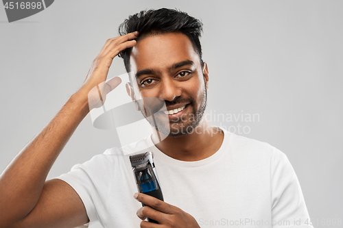 Image of smiling indian man with trimmer touching his hair