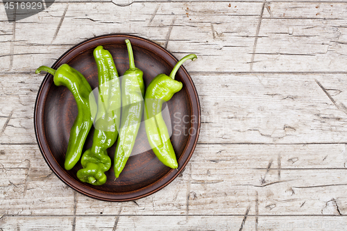 Image of Fresh green raw peppers on brown ceramic plate on rustic wooden 