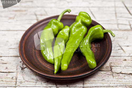 Image of Fresh green raw peppers on brown ceramic plate on rustic wooden 