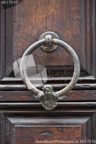 Image of Ancient italian door knocker on wooden brown door.