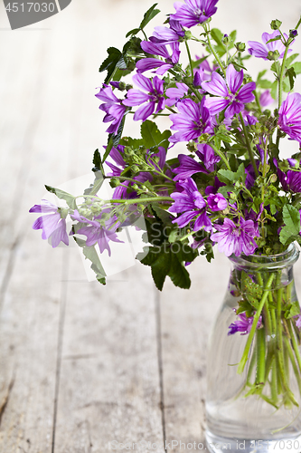 Image of Wild violet flowers in glass bottle on rustic wooden table backg