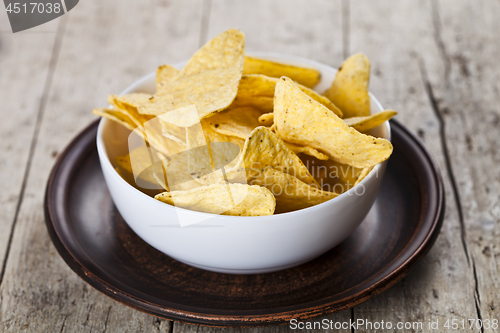 Image of Mexican nachos chips in white bowl on brown ceramic plate.