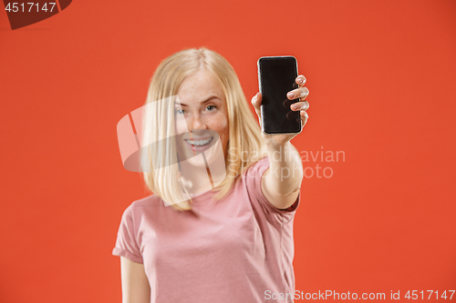 Image of Portrait of a confident casual girl showing blank screen mobile phone isolated over red background