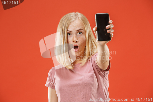 Image of Portrait of a confident casual girl showing blank screen mobile phone isolated over red background