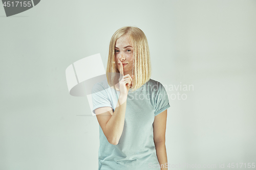 Image of The young woman whispering a secret behind her hand over gray background