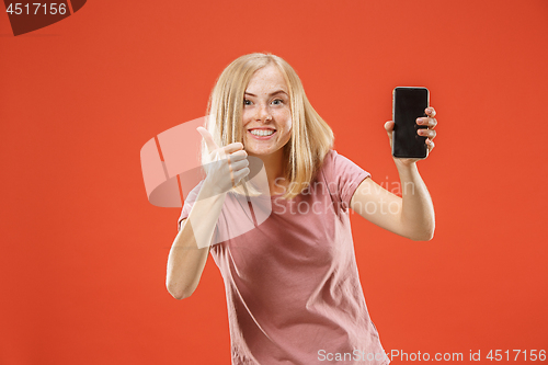 Image of Portrait of a confident casual girl showing blank screen mobile phone isolated over red background