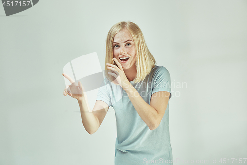 Image of The young woman whispering a secret behind her hand over gray background