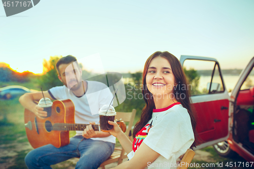 Image of Couple sitting and resting on the beach playing guitar on a summer day near river