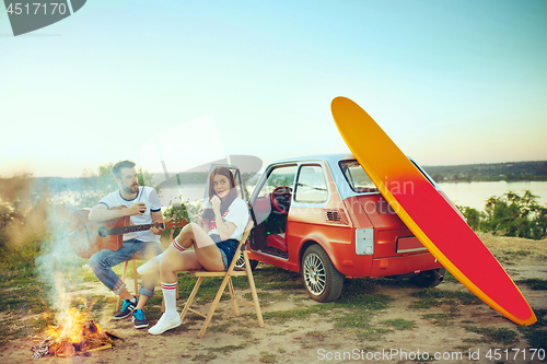 Image of Couple sitting and resting on the beach playing guitar on a summer day near river