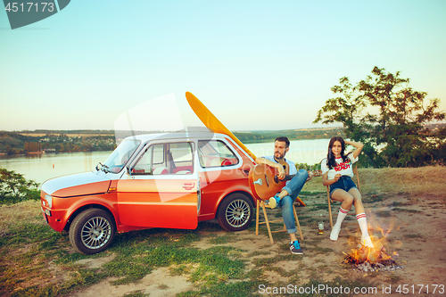 Image of Couple sitting and resting on the beach playing guitar on a summer day near river