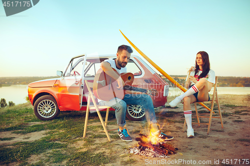 Image of Couple sitting and resting on the beach playing guitar on a summer day near river