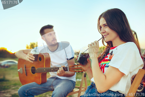 Image of Couple sitting and resting on the beach playing guitar on a summer day near river
