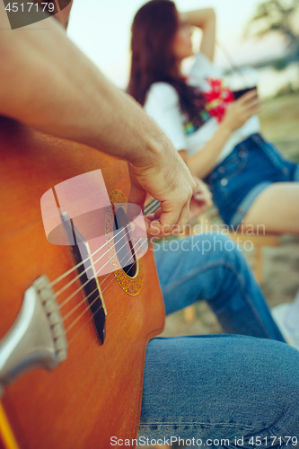 Image of Couple sitting and resting on the beach playing guitar on a summer day near river
