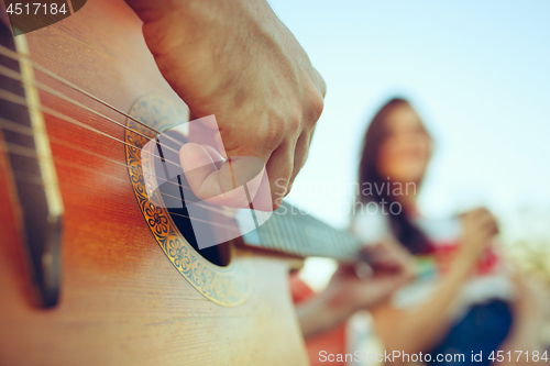 Image of Couple sitting and resting on the beach playing guitar on a summer day near river