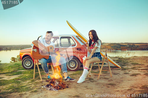 Image of Couple sitting and resting on the beach playing guitar on a summer day near river