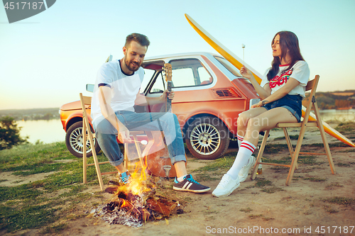 Image of Couple sitting and resting on the beach playing guitar on a summer day near river