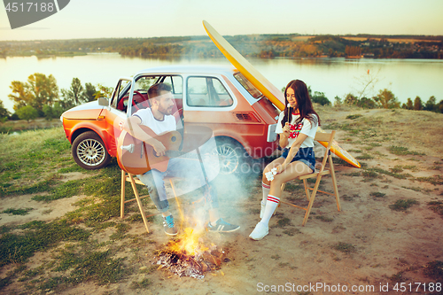 Image of Couple sitting and resting on the beach playing guitar on a summer day near river