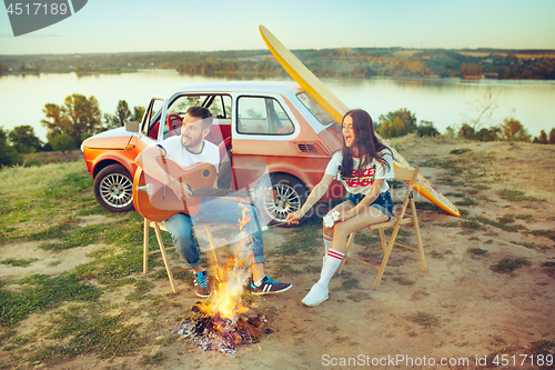 Image of Couple sitting and resting on the beach playing guitar on a summer day near river