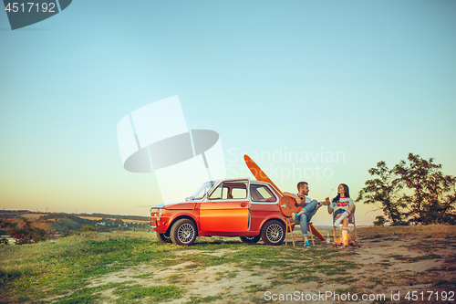 Image of Couple sitting and resting on the beach playing guitar on a summer day near river