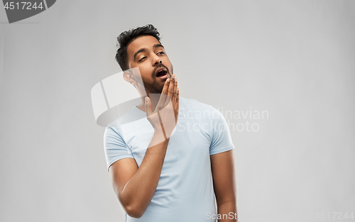 Image of tired indian man yawning over grey background