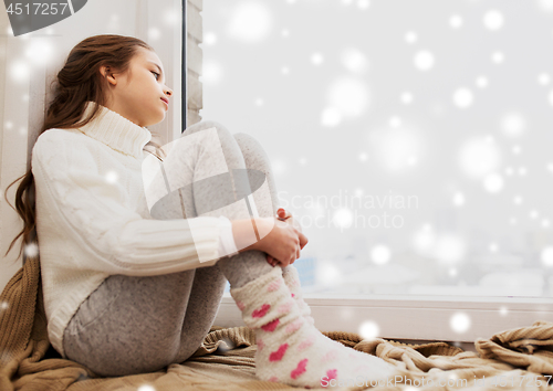 Image of sad girl sitting on sill at home window in winter