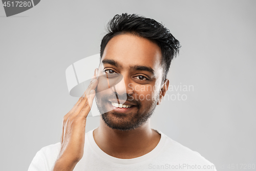 Image of smiling indian man touching his face