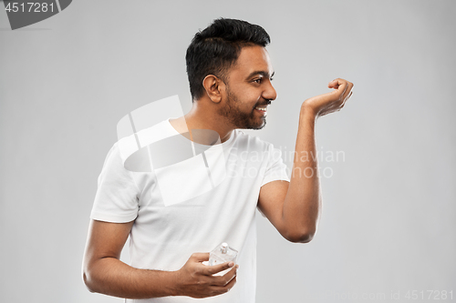 Image of happy indian man with perfume over gray background