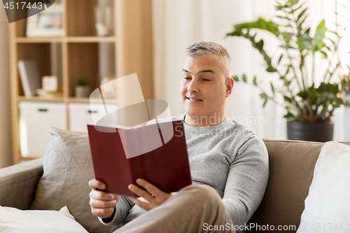 Image of man sitting on sofa and reading book at home