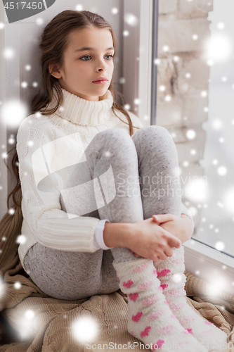 Image of sad girl sitting on sill at home window in winter