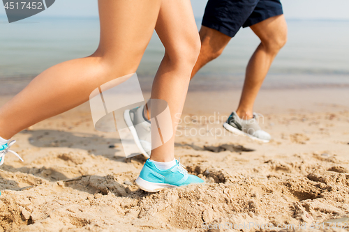 Image of legs of sportsmen in sneakers running along beach