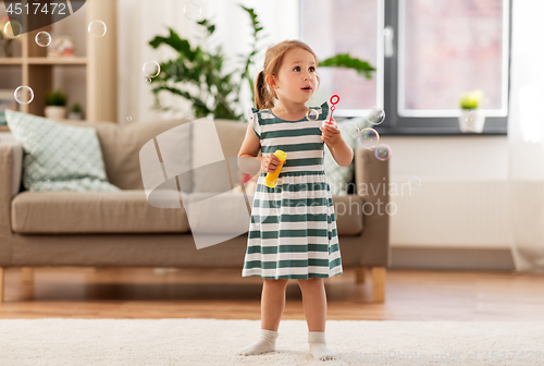 Image of little girl blowing soap bubbles at home